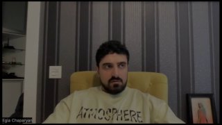 Егиа Чапарян сидит в кресле на фоне вертикальных полосатых обоев во время записи подкаста — крупный план, нейтральная обстановка.