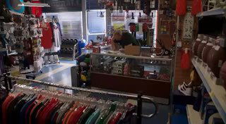 Интерьер магазина с одеждой и спортивными товарами: прилавки, вешалки с футболками и стеллажи с обувью и аксессуарами на заднем плане, общий план.