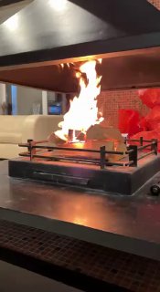 Пылающий камин в интерьере загородного дома: огонь на подставке, теплый свет и уютная мебель рядом, создают атмосферу тепла и отдыха.