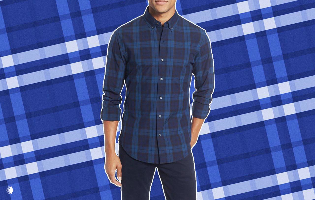 Мужская модель в тёмно‑синей клетчатой фланелевой рубашке на декоративном фоне с крупным синим узором, вид по пояс.
