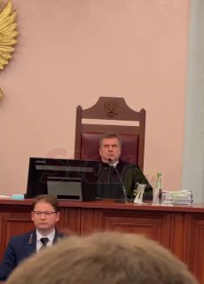 Судебный зал: судья в мантии сидит за кафедрой в зале суда, видны столы с документами и присутствующие — кадр во время оглашения решения