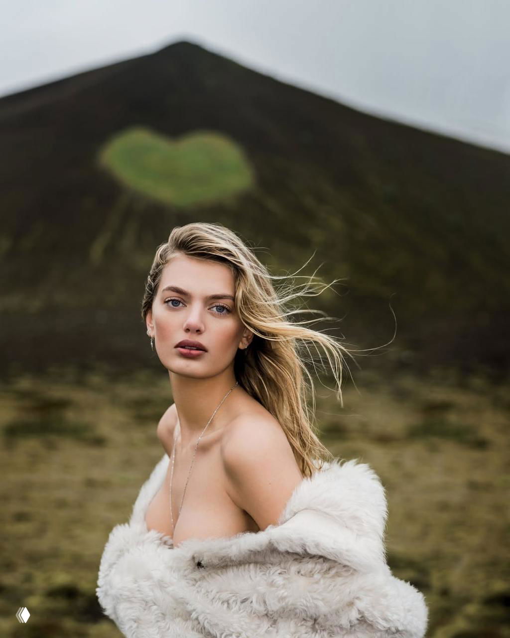 Портрет на фоне холма с сердцевидным островком зелени: модель частично обнажена, развевающиеся волосы и мягкий ветер в кадре создают романтичное настроение.