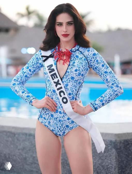 Женщина в голубом купальнике с ленточкой «Mexico» на фоне сцены конкурса красоты — полный рост, официальный кадр финала шоу, поза стоя.
