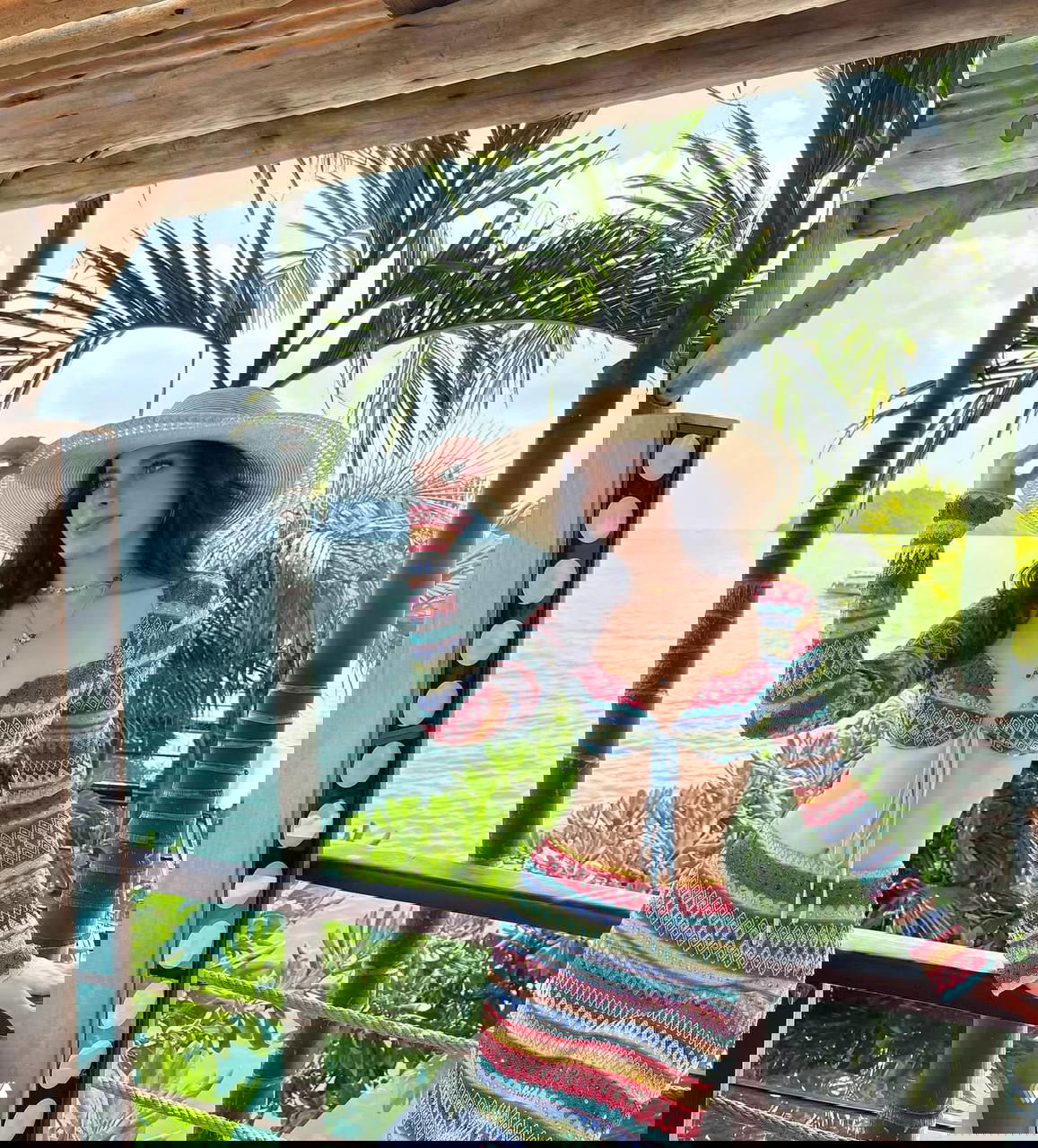 Женщина в разноцветном вязаном костюме и соломенной шляпе у моря и пальм — отпускная фотосъёмка в курортной локации, полный рост.