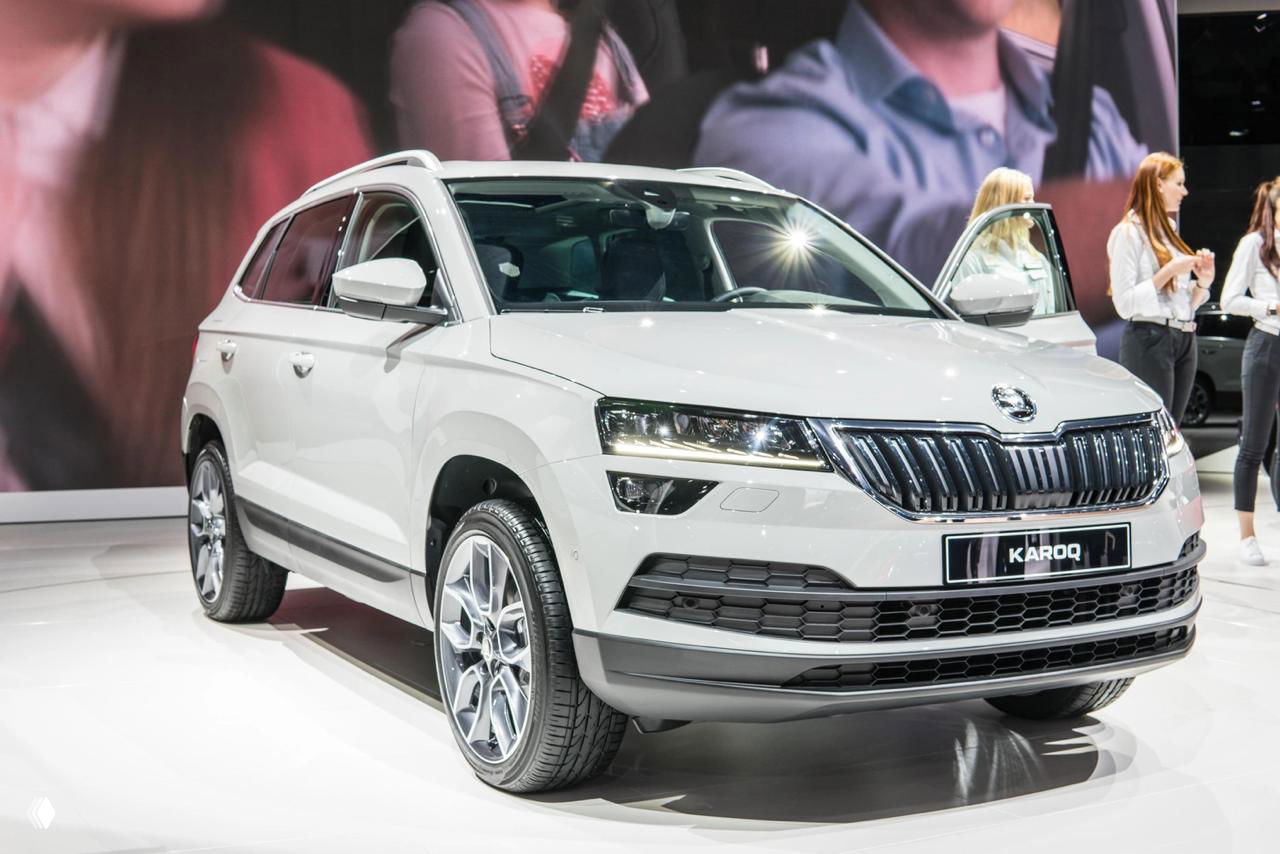 Белый Skoda Karoq на стенде, вид спереди; подчёркнуты фары, решётка и спокойная внешность — компактный и рациональный кроссовер