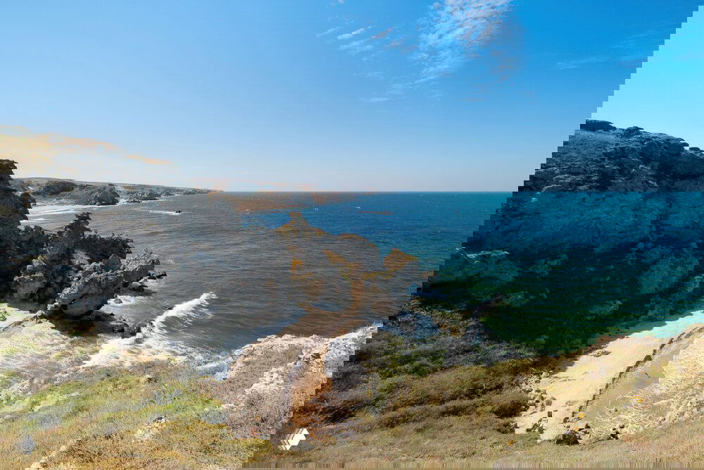 Панорамный вид крымского пляжа с бирюзовым морем и скалистыми обрывами, песочная бухта внизу и прибрежная растительность — кадр Андрея из Крыма.