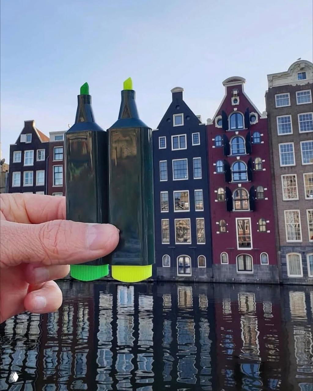 Палец и пара маркеров на переднем плане создают ассоциативную иллюзию высоких башен рядом с традиционными фасадами амстердамских домов у канала.