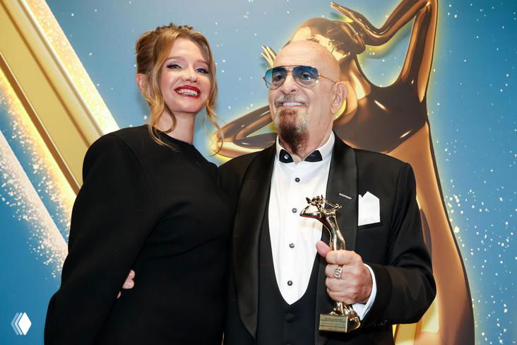 Михаил Шуфутинский и Светлана Уразова позируют вместе на официальном мероприятии: артист в смокинге держит награду, рядом улыбающаяся супруга.