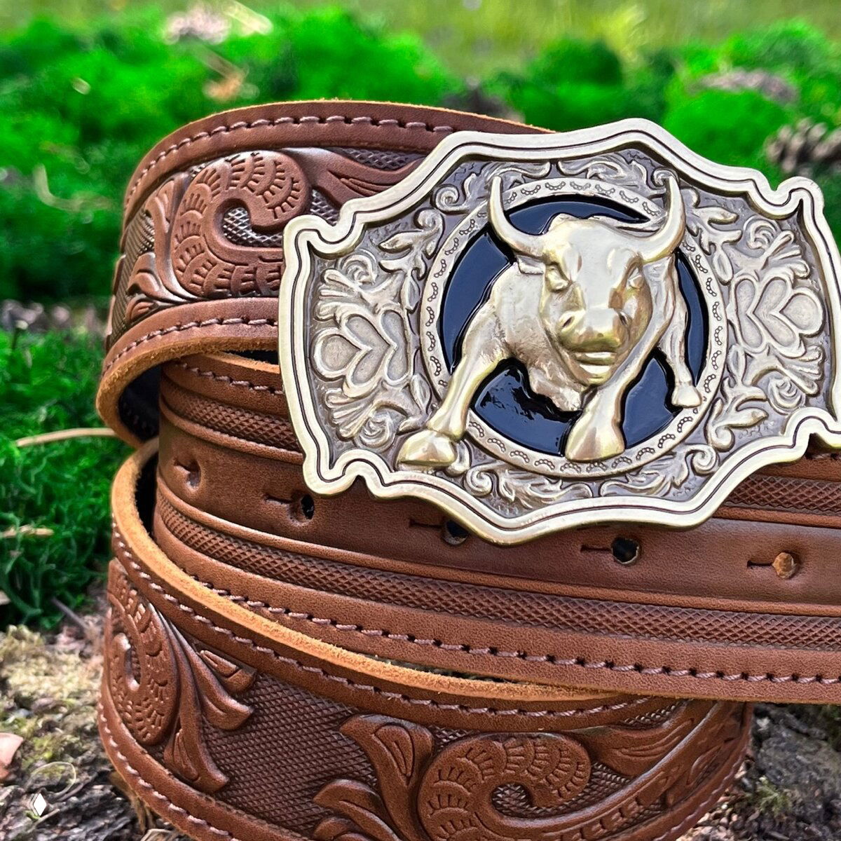 Коричневый кожаный ремень с тиснением в виде растительных мотивов и крупной бронзовой пряжкой с изображением быка на декоративном фоне.