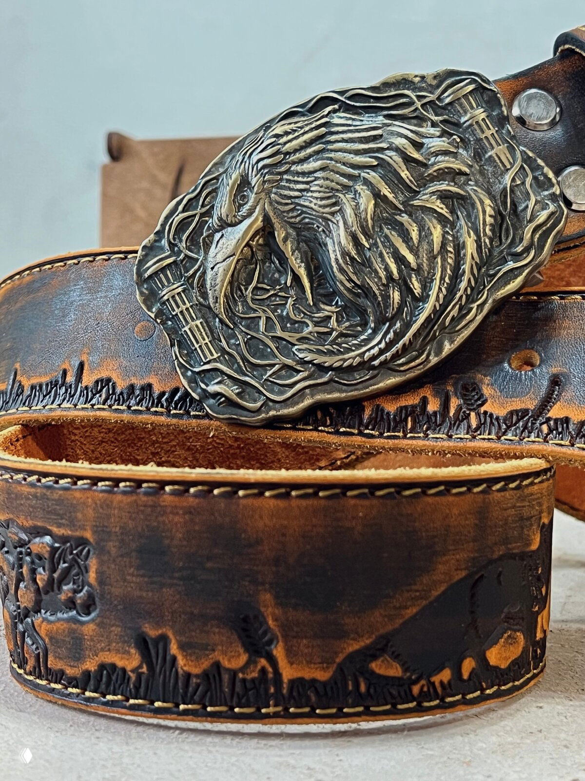 Крупный план тиснёного кожаного ремня коричневого цвета с изображением животных на бортике и контрастной строчкой — текстура и края ремня видны детально.
