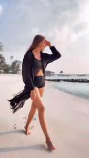 Любовь Толкалина в купальнике идёт по песчаному пляжу у моря, видны пальмы и берег — кадр из тёплого отпускного видео актрисы.