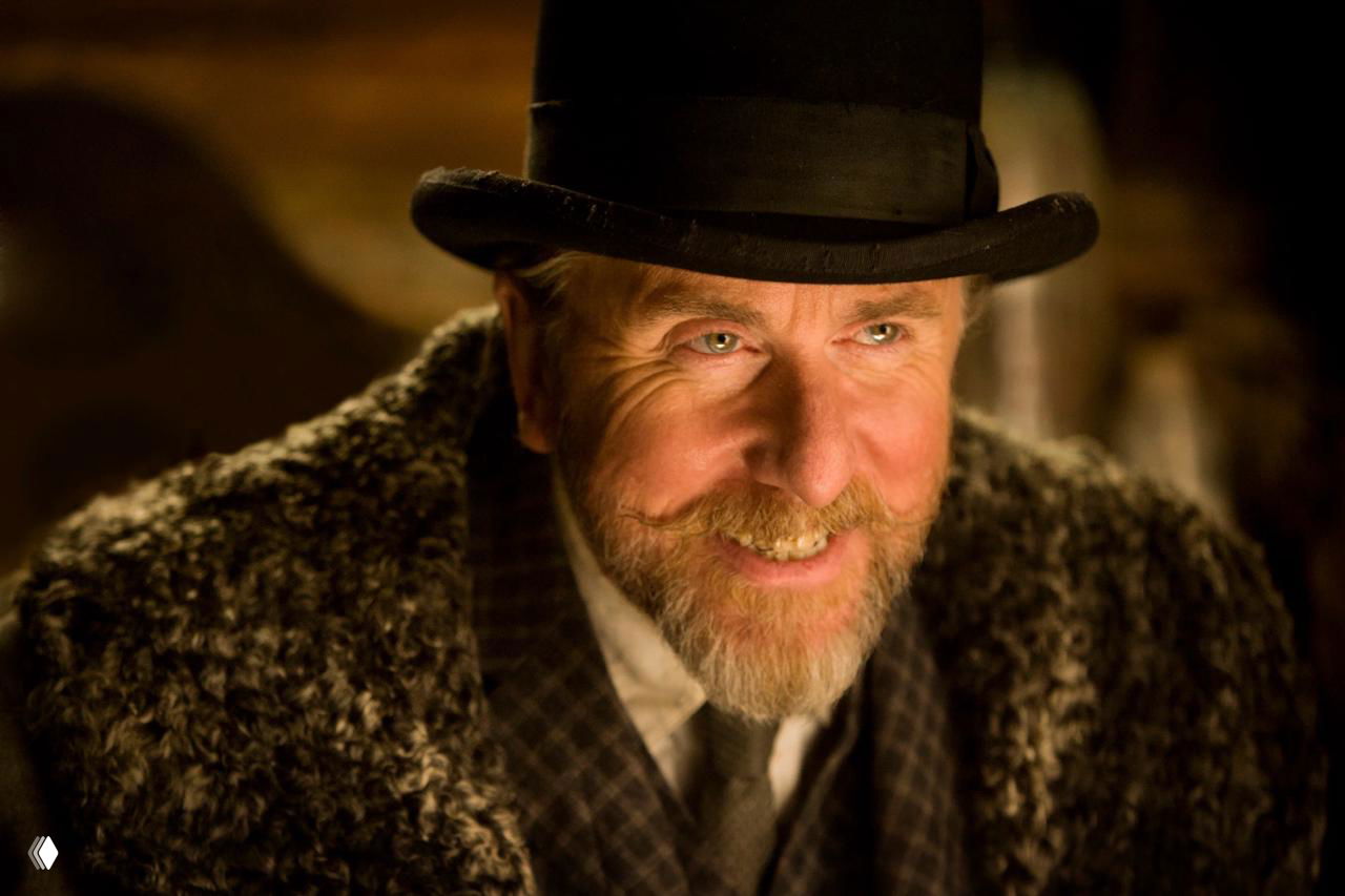 Портрет героя в шляпе и меховой одежде из фильма «Омерзительная восьмерка», крупный план лица с улыбкой и хитрым выражением в кадре.