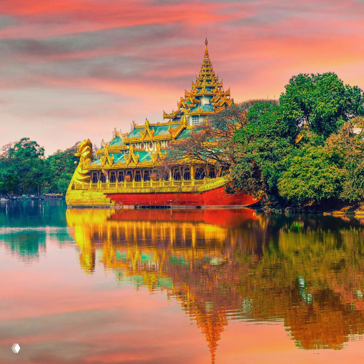 Золотистое тайское строение на воде при закате, с ярким отражением в озере и зелёными деревьями на берегу.