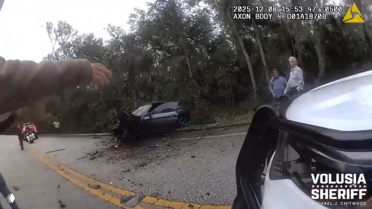 Вид с нагрудной камеры полиции на разбитый тёмный кабриолет BMW на обочине дороги, офицеры и обломки вокруг; на экране виден таймштамп.