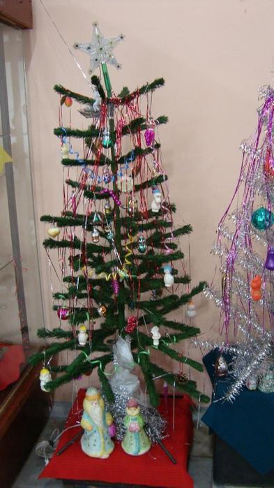 Каркасная ёлка с редкими ветками, украшенная мишурой и пластиковыми игрушками; фото подчёркивает скромность праздничного декора в ряде квартир.