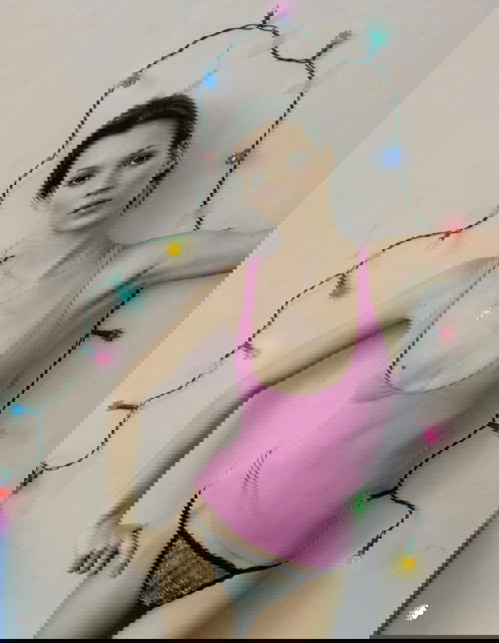 Модель в розовой майке и черных кружевных трусиках на фоне гирлянды лампочек, студийная композиция в стиле 90-х.