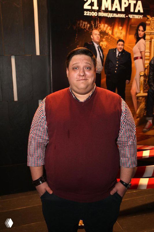 Роман Попов в повседневной одежде на мероприятии — полный рост актера на фоне афиши сериала «Полицейский с Рублевки», настроение красной дорожки.