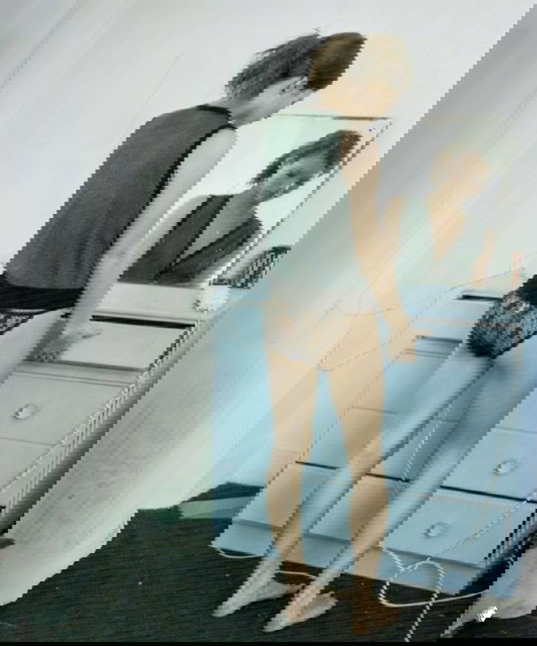 Молодая модель стоит у голубого комода в кружевных трусиках, вид со спины и отражение в настольном зеркале.