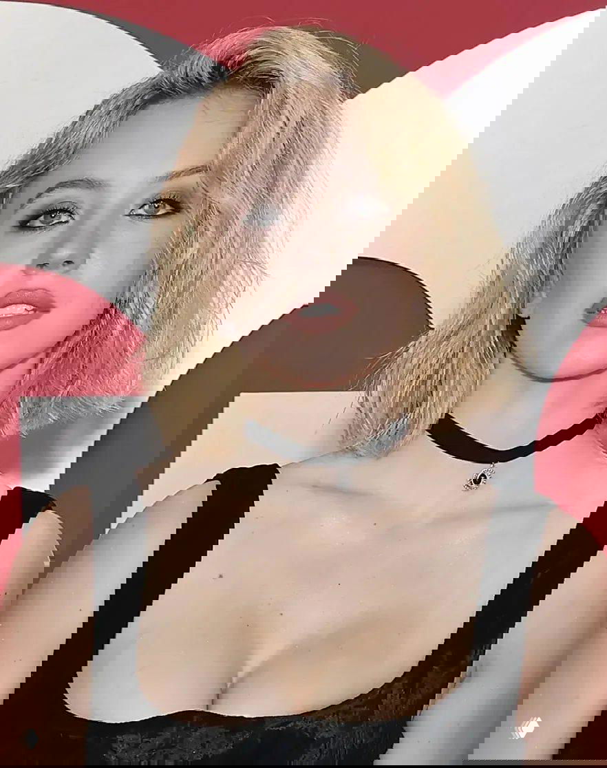 Крупный план женщины с короткой светлой причёской и выразительным макияжем в чёрном платье с глубоким декольте на фоне логотипа GQ.