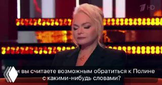 Крупный план певицы в телевизионной студии: серьёзное выражение лица, светящийся фон сцены и субтитры в нижней части кадра.