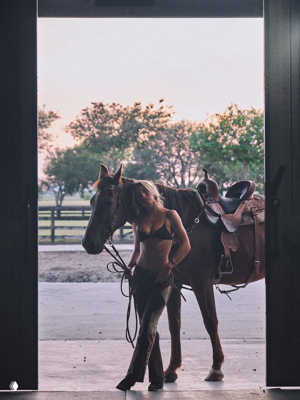 Силуэт и фигура в дверном проёме конюшни: модель ведёт лошадь, дневной свет за пределами стойла создаёт контраст силуэтов.