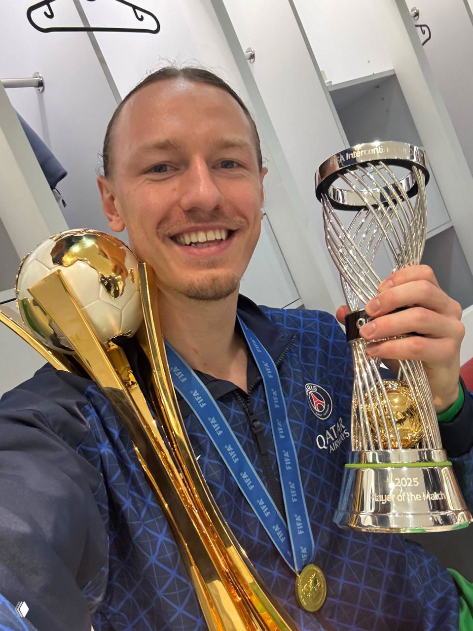Матвей Сафонов в форме ПСЖ улыбается в камеру, держит два трофея и медаль после победы в Межконтинентальном кубке.