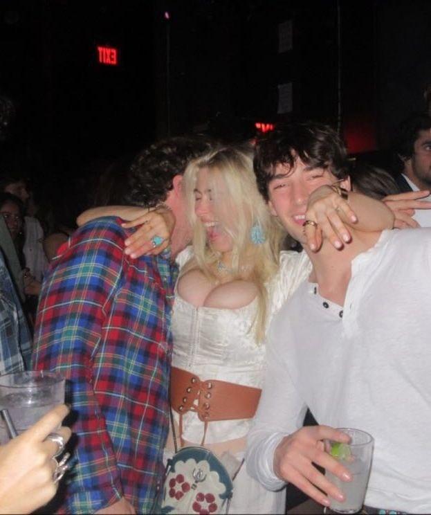 Ночная сцена в клубе: молодая женщина в светлом корсете окружена друзьями и обнимается с гостями праздника