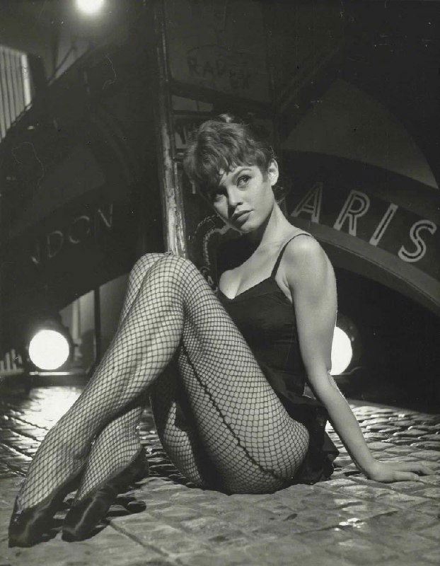 Чёрно-белая фотография молодой Бриджит Бардо в театральном образе с сетчатыми чулками, кадр из фотосессии на съёмочной площадке.
