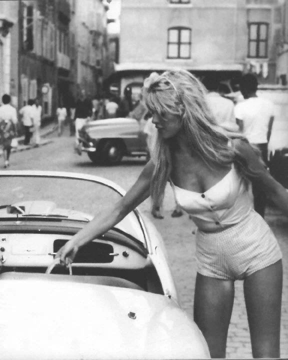 Архивная чёрно-белая уличная фотография Бриджит Бардо у ретро-автомобиля, кадр в повседневном образе из молодости актрисы.