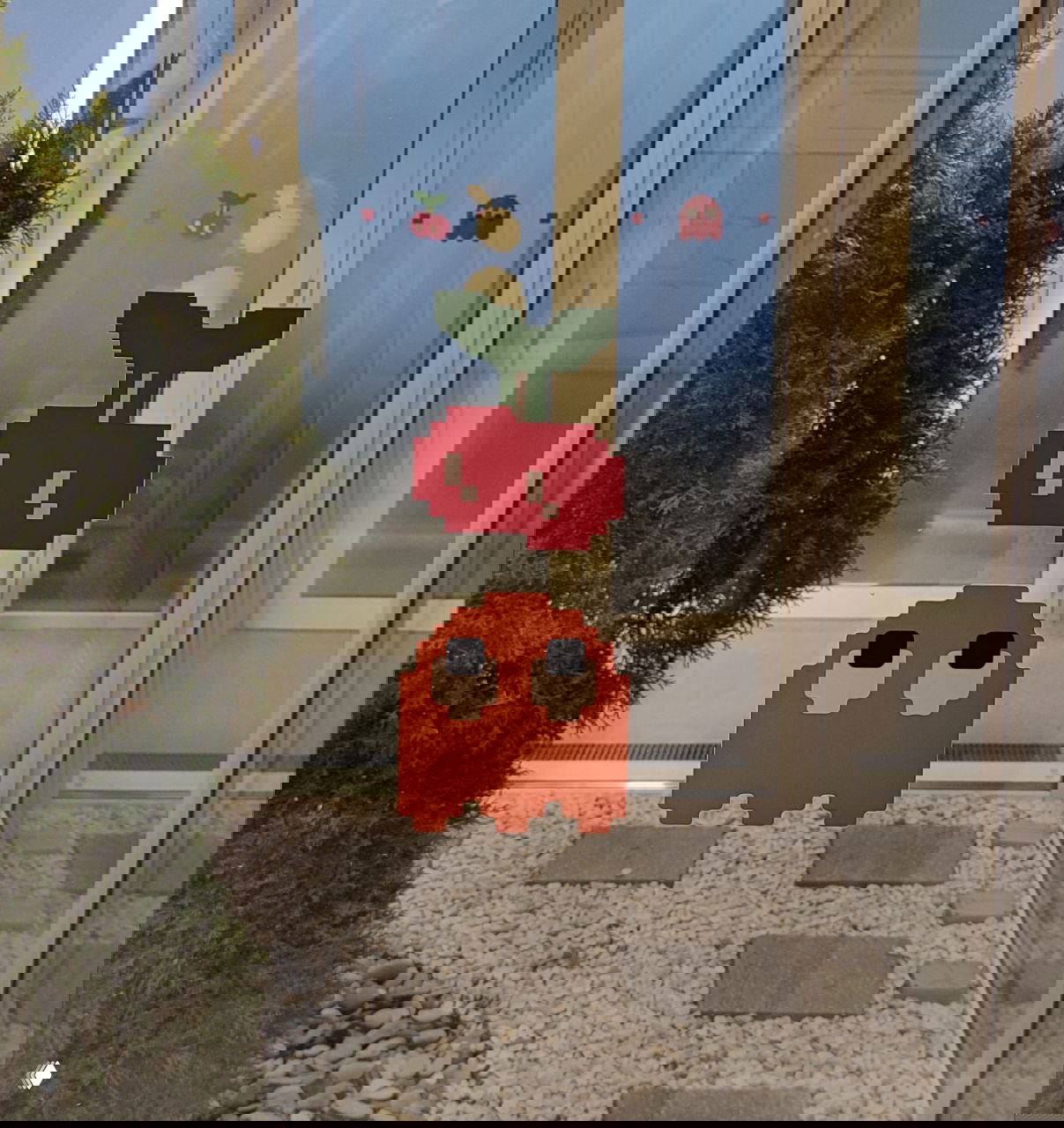 Пиксельные изображения (привидение и ягоды) на стекле корпуса кампуса Неймарка; перед ними декоративная гравийная отсыпка и зелёные туи.