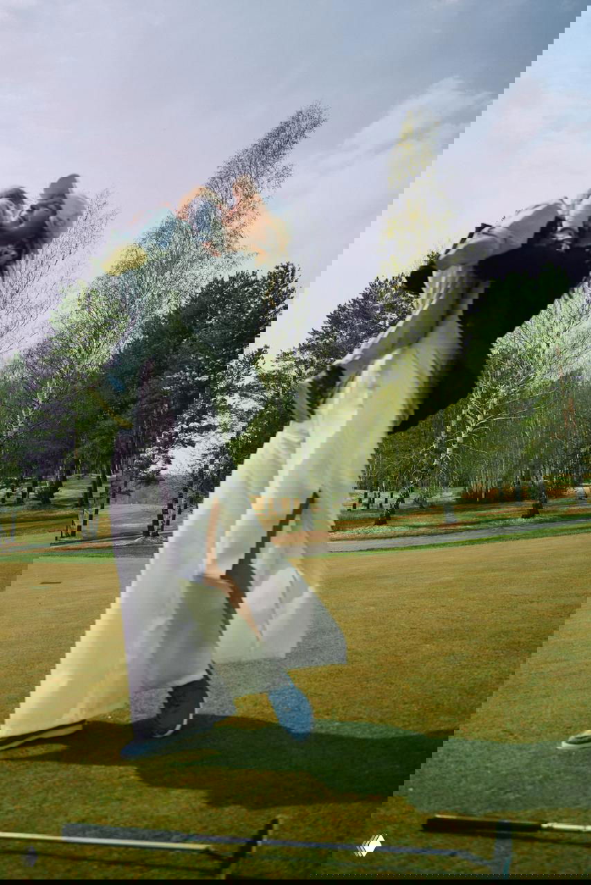 Женщина в белых палаццо и кепке поднимает малыша на зелёном поле среди берёз — семейная сцена, образ из коллекции ЛЕТОМАЙ.