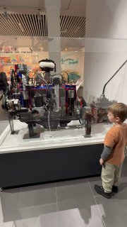 Мальчик рассматривает макет двигателя за витриной: подробный технический экспонат и внимание ребёнка к механике в музее техники.