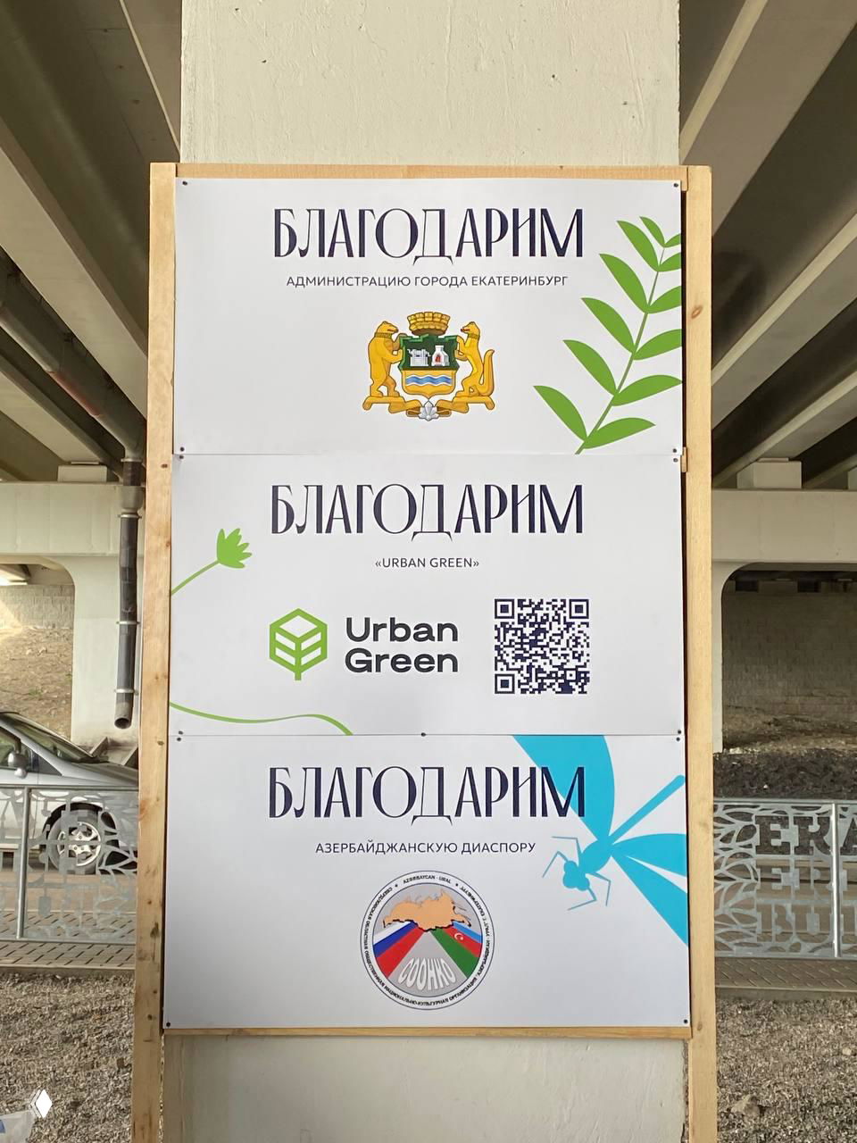 Информационная панель с надписью «БЛАГОДАРИМ», гербом Екатеринбурга и логотипами партнёров на временной конструкции в городской среде.