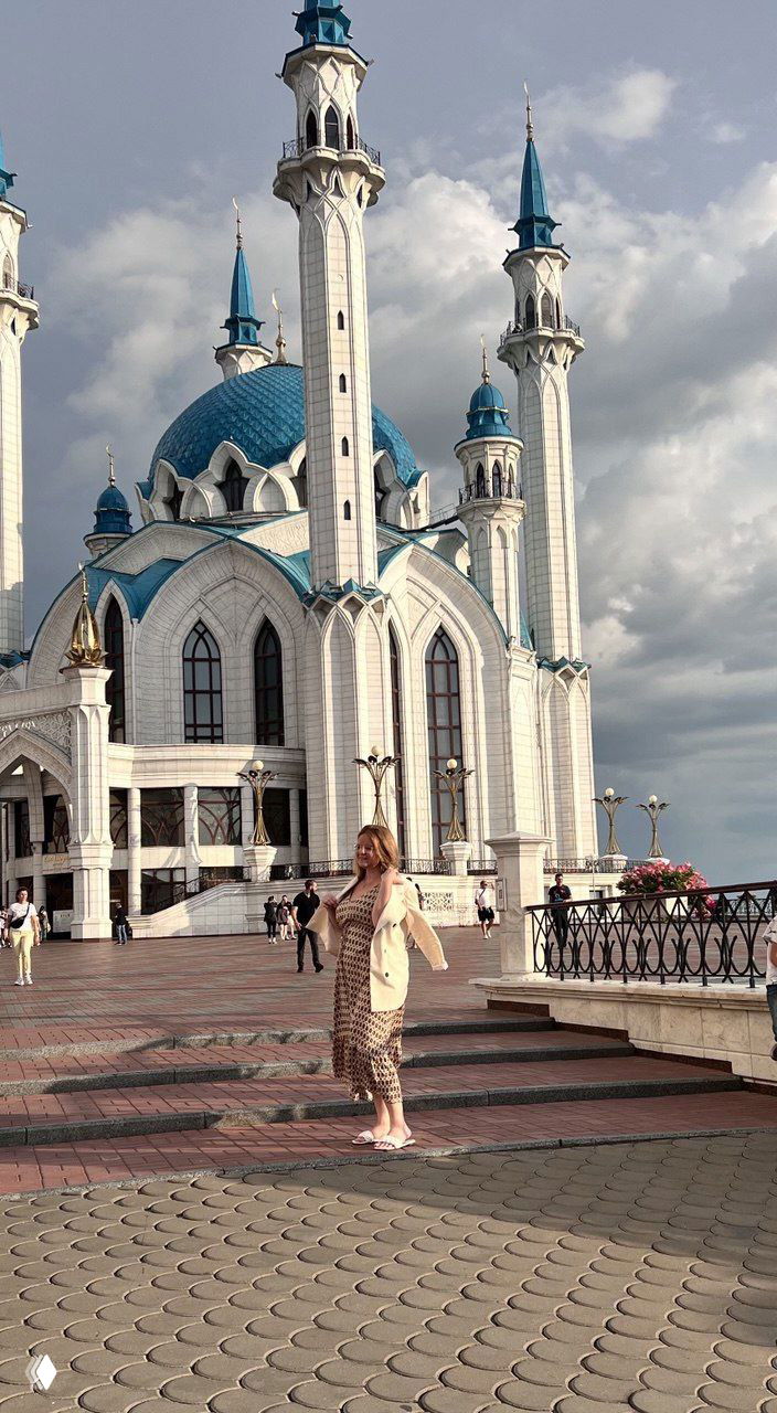 Женщина в лёгком платье стоит на набережной у мечети с бирюзовыми куполами и минаретами в Казани, светлый летний день.