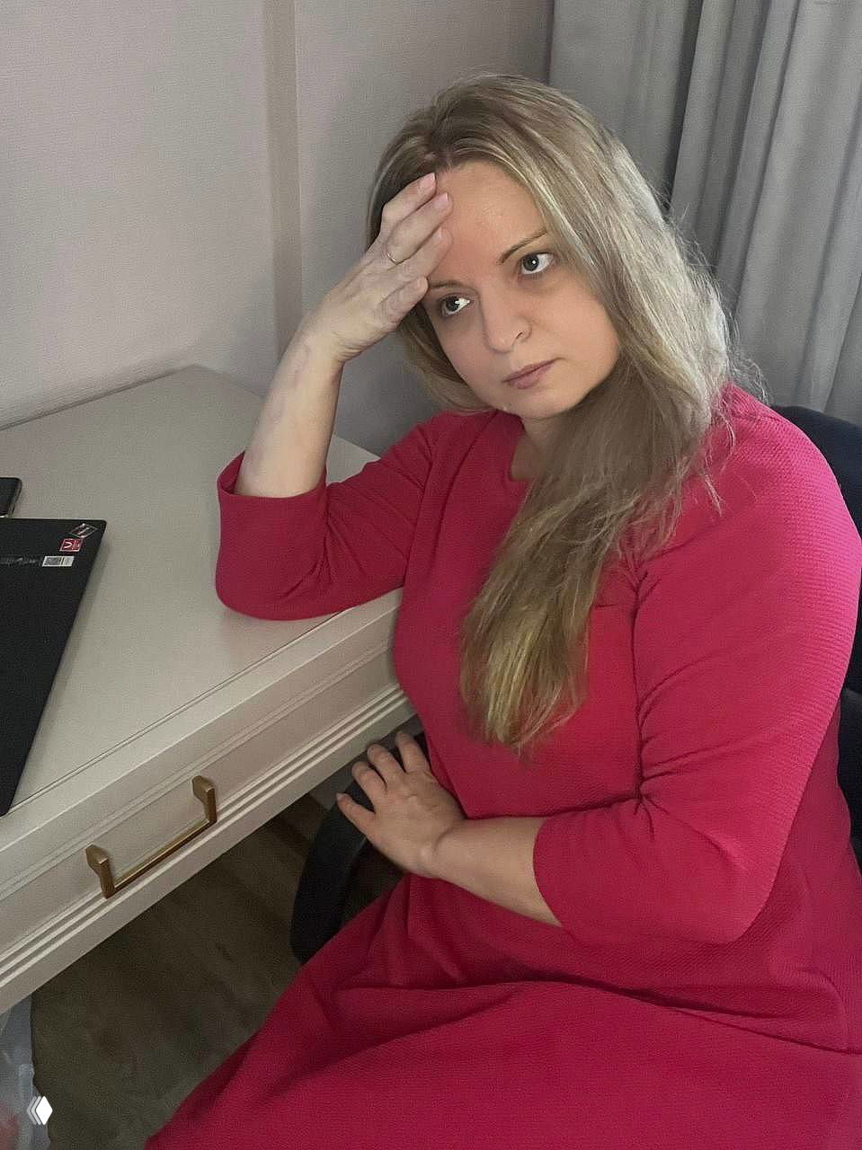 Та же женщина в красном платье с задумчивым выражением, сидит у рабочего стола; изображение иллюстрирует ситуацию бухгалтера при проверке зарплат.