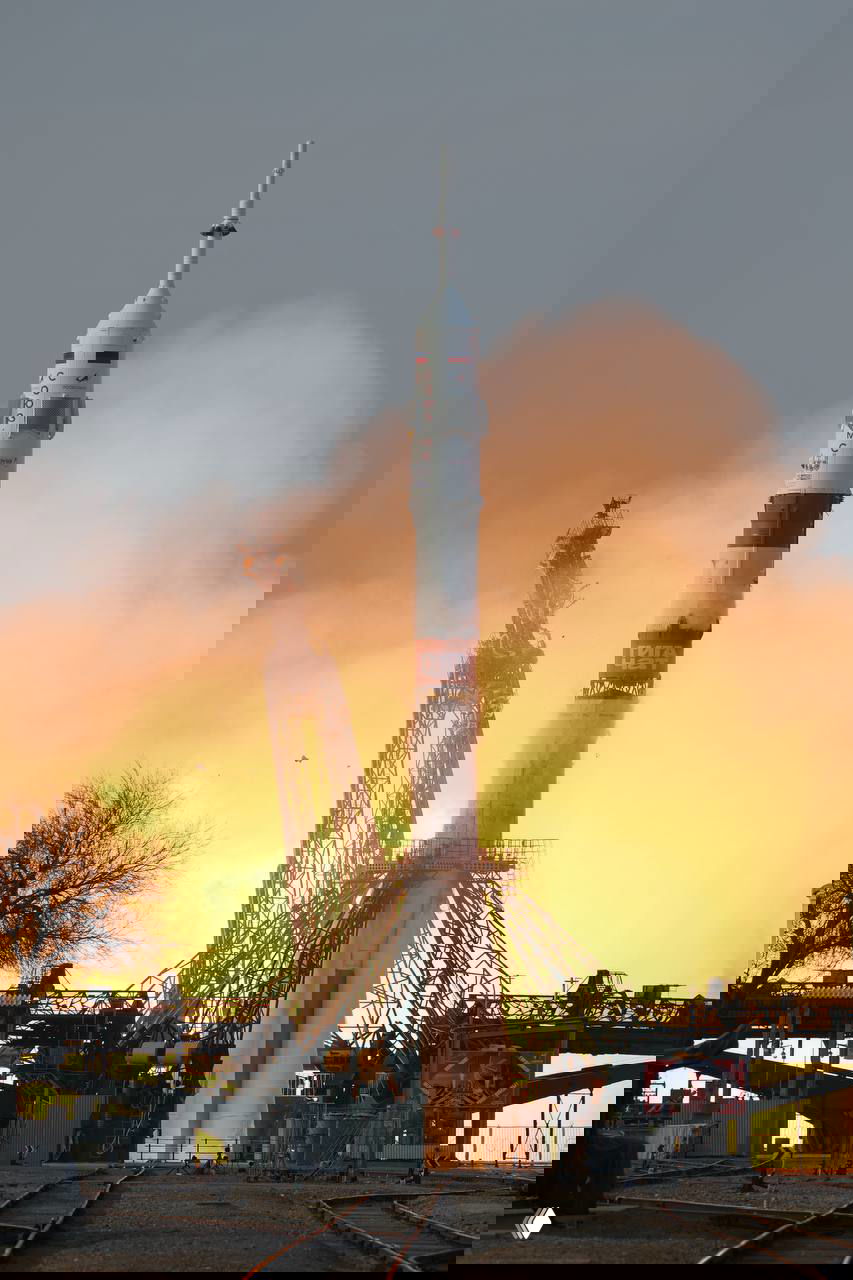 Ракета «Союз» на стартовом столе на Байконуре в момент включения двигателей: яркое пламя у основания и технические конструкции вокруг.