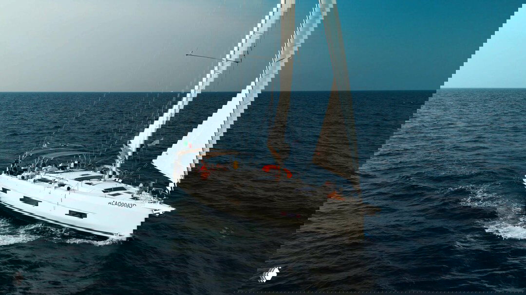 Аэровид сверху на белую парусную яхту, идущую по открытому морю; вид подчёркивает размеры судна и спокойное синее море вокруг.