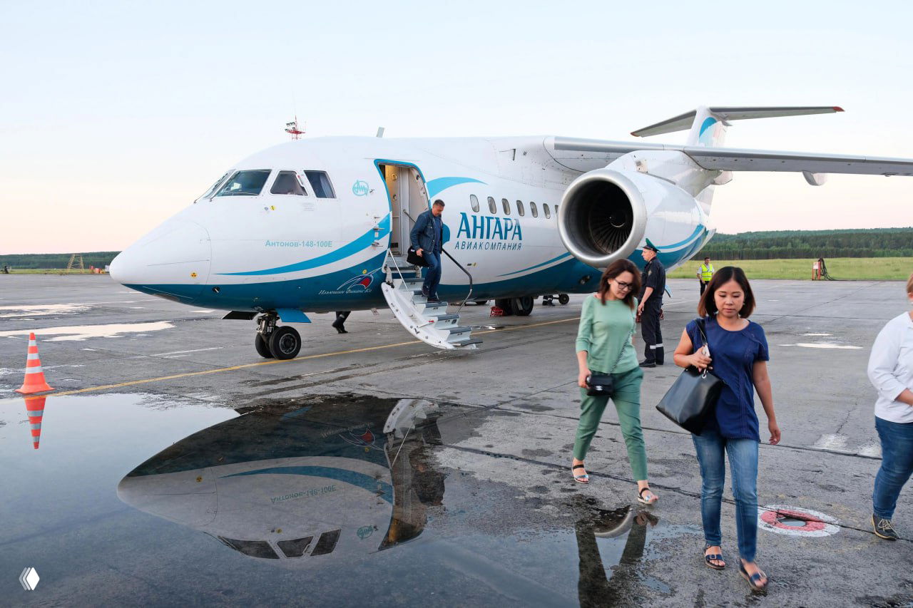 Пассажиры покидают самолёт авиакомпании «Ангара» на перроне; видно фюзеляж с логотипом, открытые трап и отражение воздушного судна на мокрой поверхности.