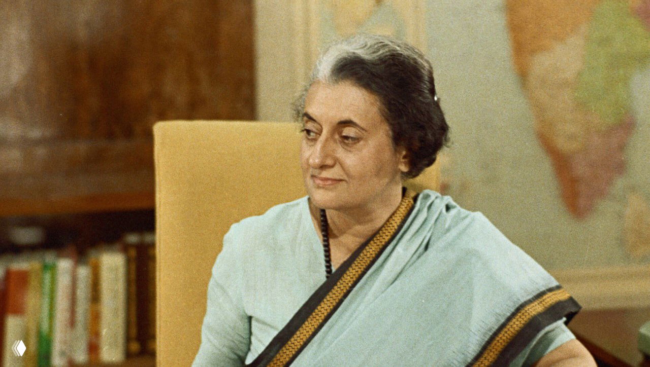 Цветной архивный снимок женщины-политика в кабинете на фоне карты мира и книжных полок, официальный рабочий портрет.