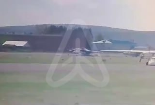 Кадр с видеозаписи инцидента на аэродроме: вдалеке видна взлётно-посадочная полоса и стоянка самолётов, смазанные силуэты техники и строений рядом с полосой.