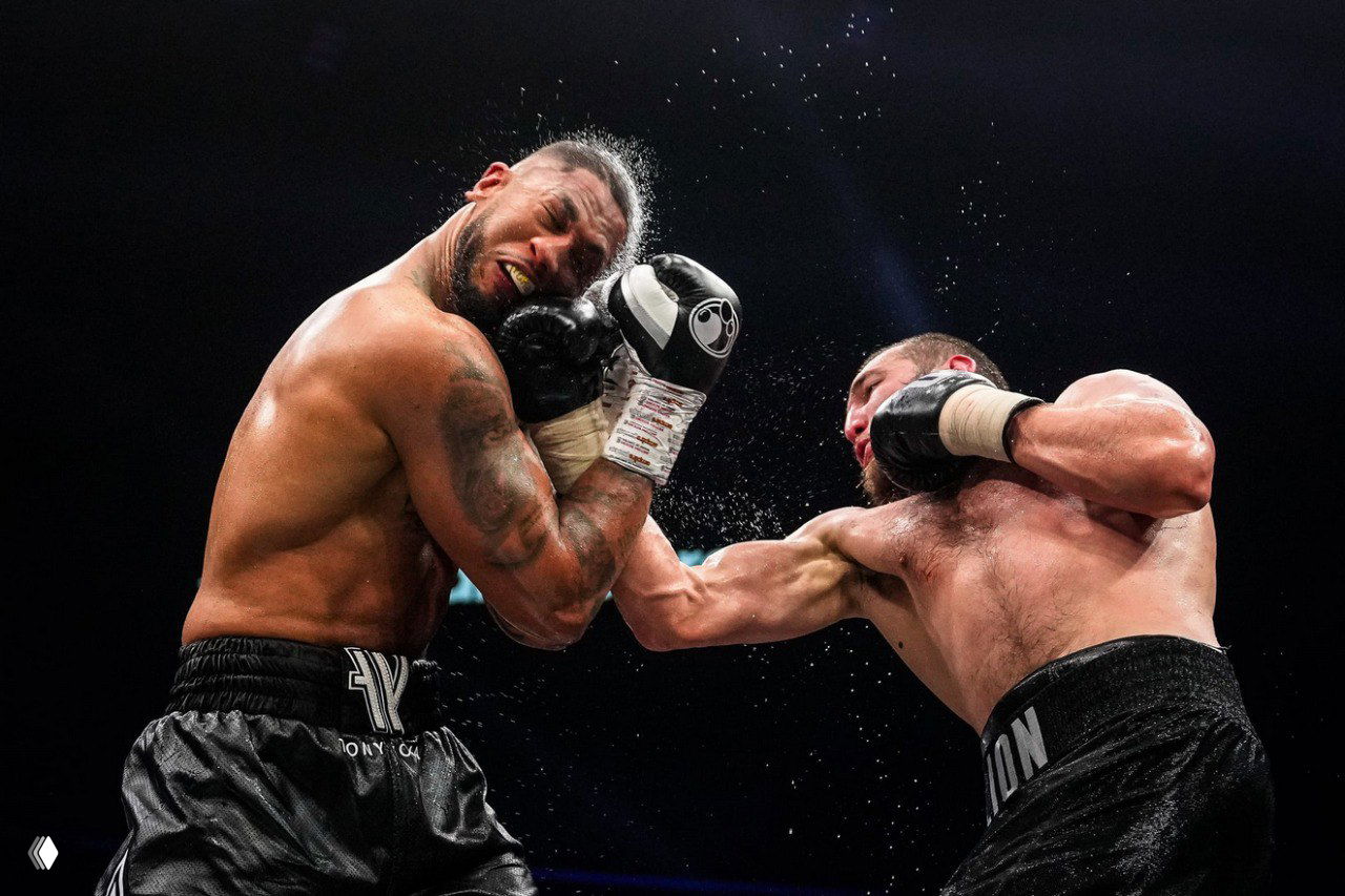 Боксёрский поединок в момент удара: два боксера, капли пота и интенсивность контакта, динамичный и эмоциональный снимок из подборки победителей конкурса.