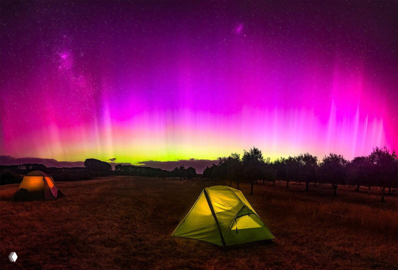 Морской берег с двумя каменными останцами, над которыми вертикально возносится пурпурно‑красное полярное сияние, отражающееся в воде.