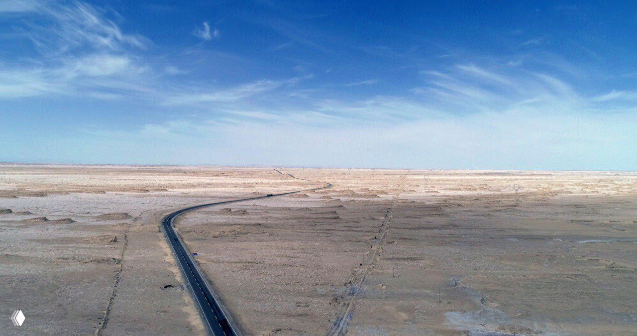 Аэрофото: шоссе тянется через обширную пустынную Цайдамскую котловину рядом с Голмудом — вид сверху на солончаковую и песчаную поверхность.