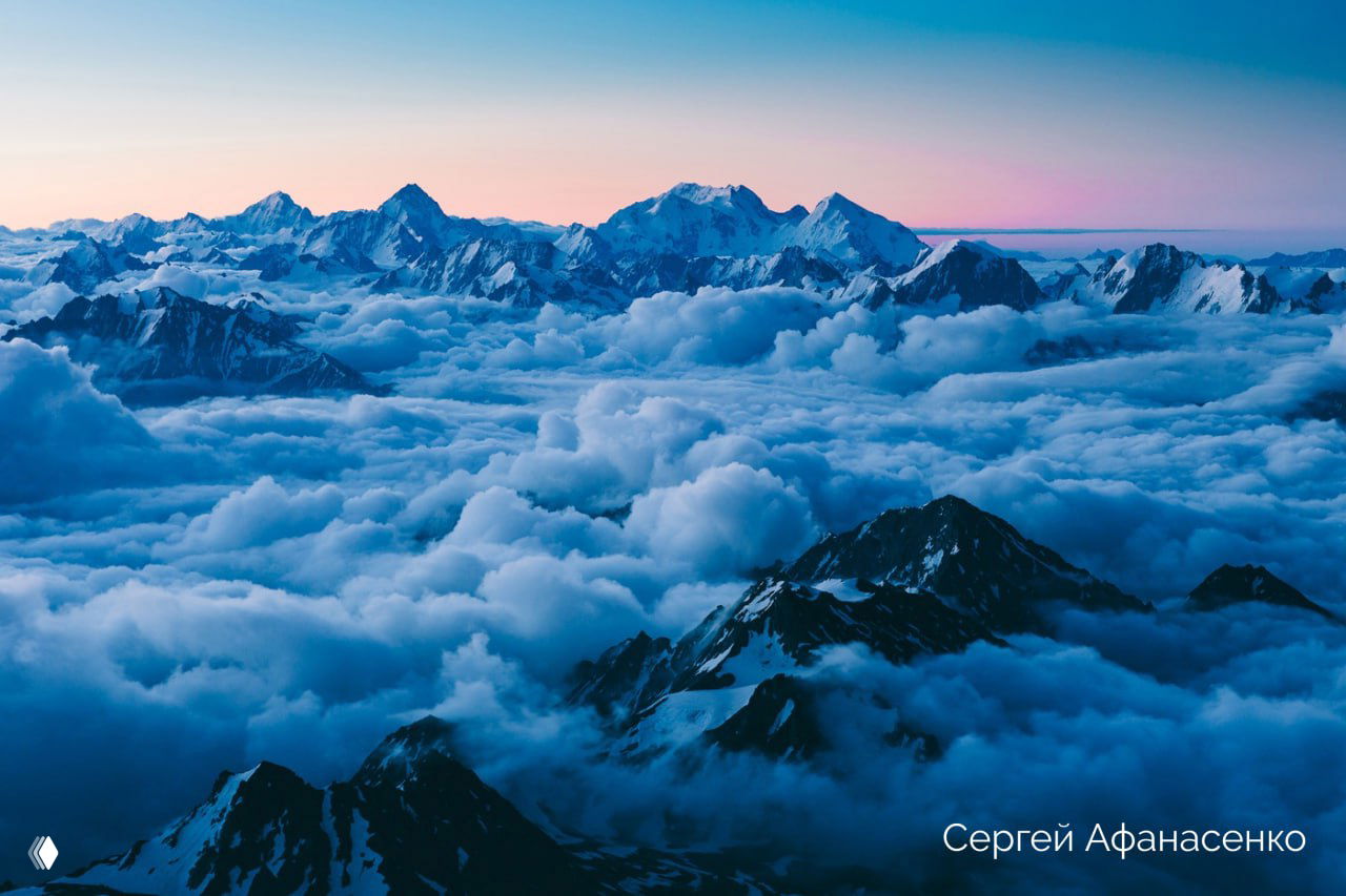 Панорамный вид на горы и море облаков над хребтом в холодных голубых тонах; кадр подчёркивает масштаб Безенгийской стены и альпийский пейзаж.