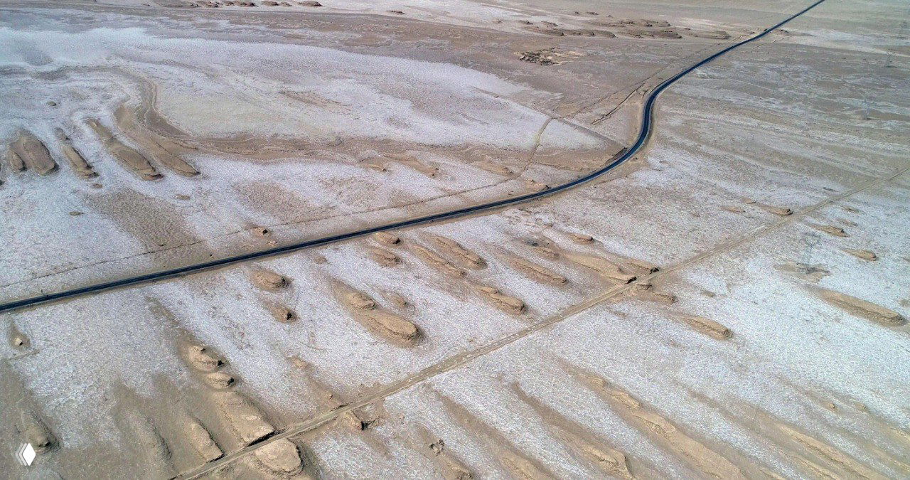 Аэрофото: изгибающийся асфальтовый путь в безводной пустыне Цайдамской котловины, с видимыми следами от ветровых форм рельефа.