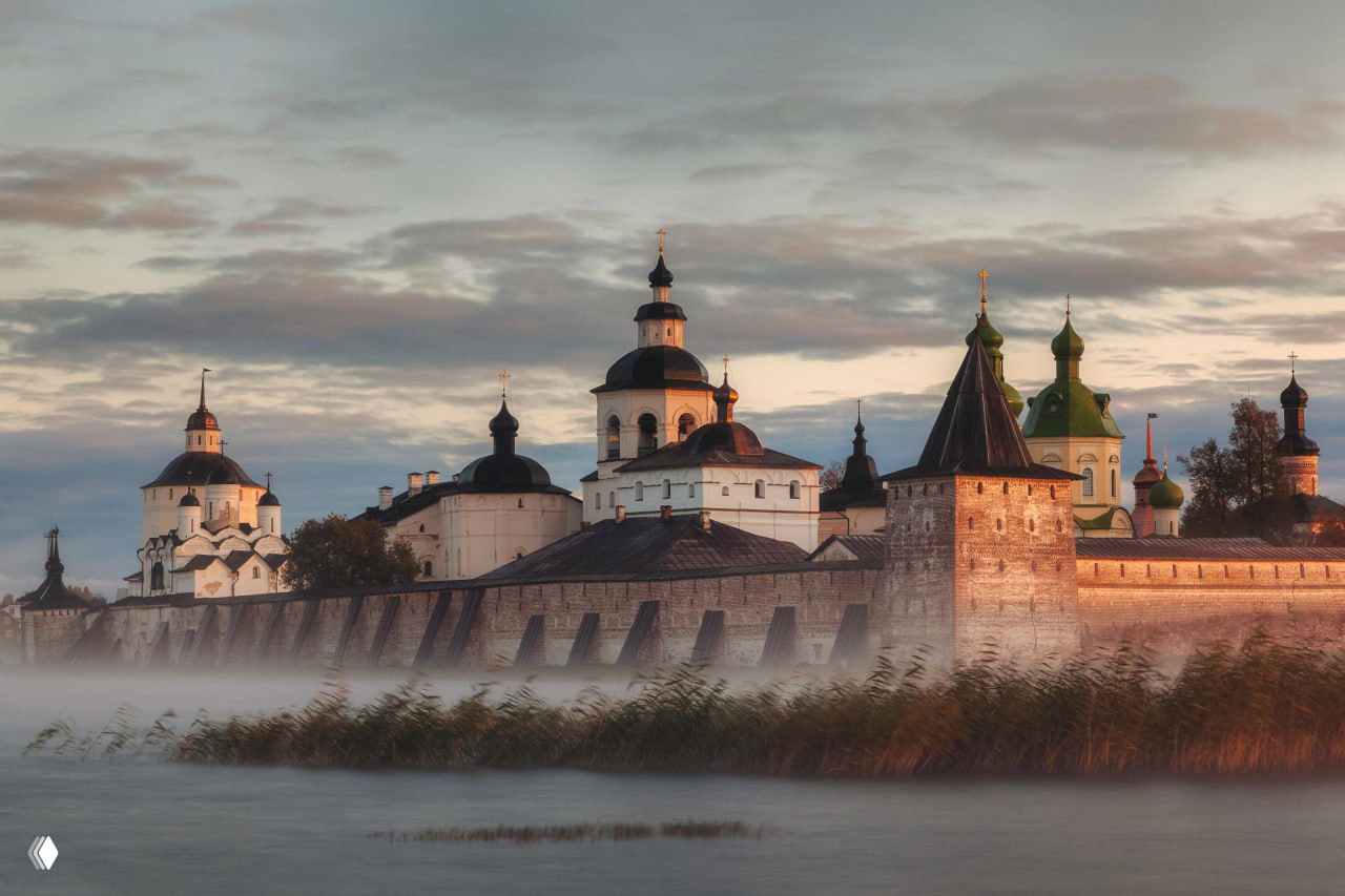 Панорамный вид на Кирилло‑Белозерский монастырь: протяжённая крепостная стена, многочисленные купола и башни на фоне Сиверского озера в лёгком тумане.