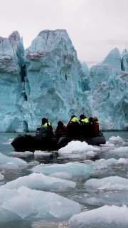 Экскурсионная резиновая лодка среди айсбергов у берегов Шпицбергена: туристы в ярких куртках рядом с плавающими льдинами и голубыми торосами.