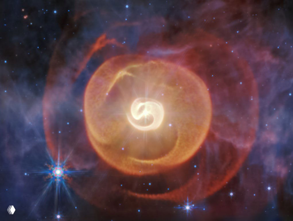 Инфракрасное изображение телескопа «Джеймс Уэбб» (камера MIRI): тройная звёздная система Апоп с ярким ядром и четырьмя спиралевидными облаками космической пыли.