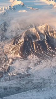 Аэрофотоснимок заснеженных гор и ледяных полей Шпицбергена — сложные хребты, ледники, тонкие полосы облаков и холодный утренний свет.