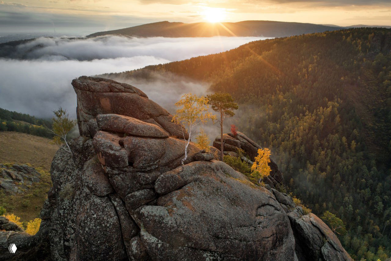Панорамный вид на скалы и утренний туман над долиной, на вершине каменные образования и редкие берёзы, рассвет над окружающим лесом